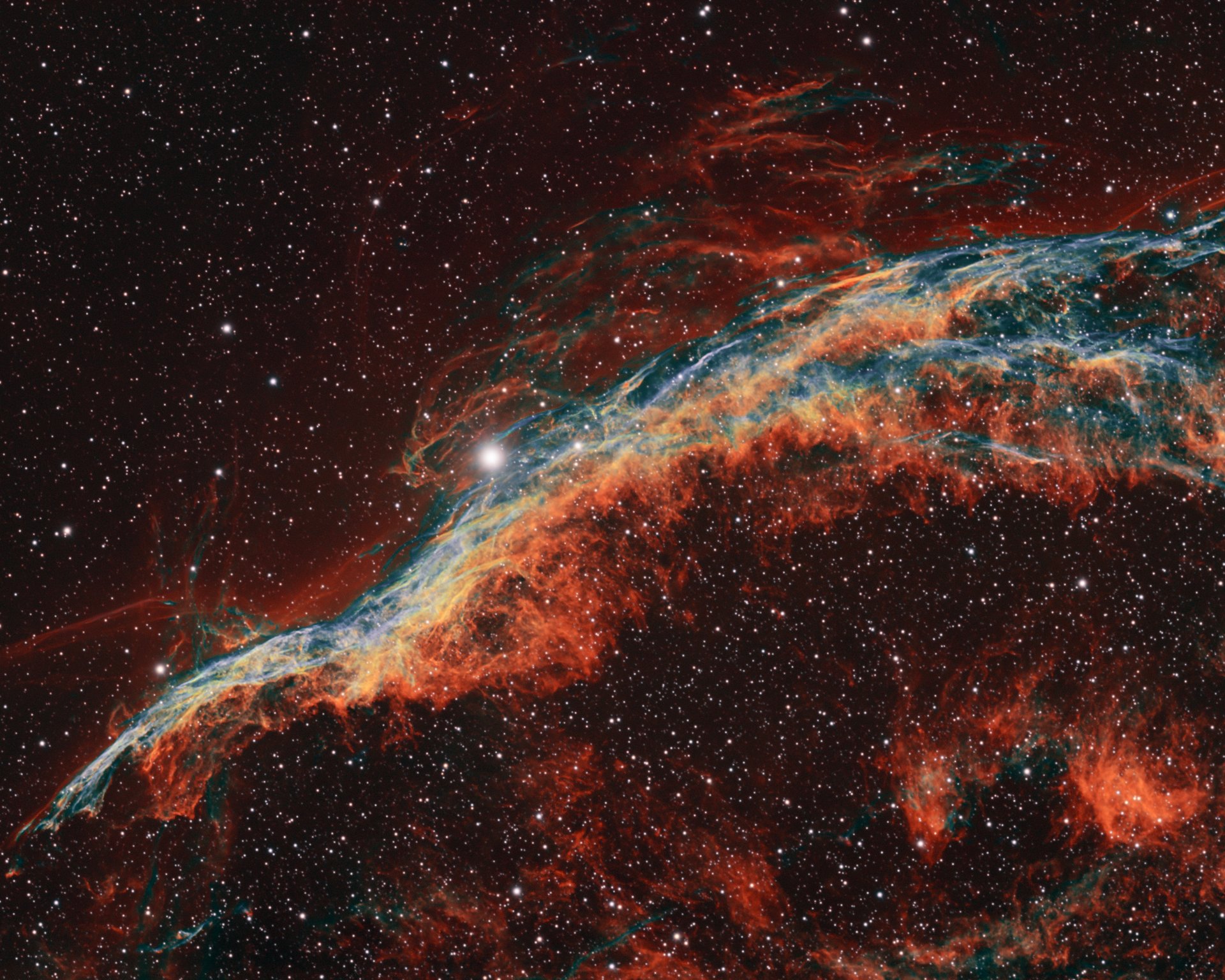 Astrophotograph of the Western Veil Nebula NGC 6960, the Witch's Broom, showing braided cyan doubly ionized oxygen and orange-red hydrogen filaments crossing the bright foreground star 52 Cygni
