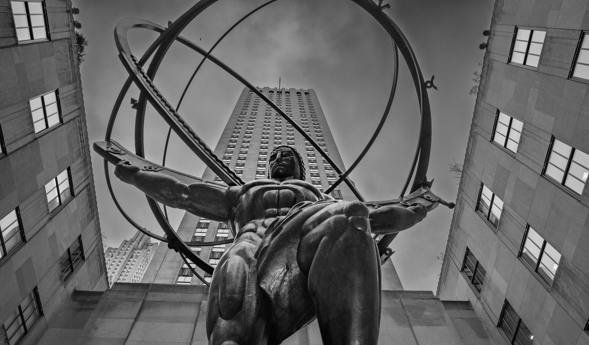 Statue of Atlas holding the world in front of skyscrapers in black and white.