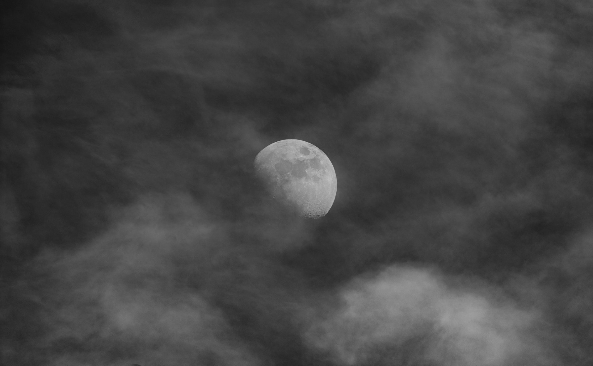 lack-and-white photograph of the Moon emerging through dramatic textured clouds