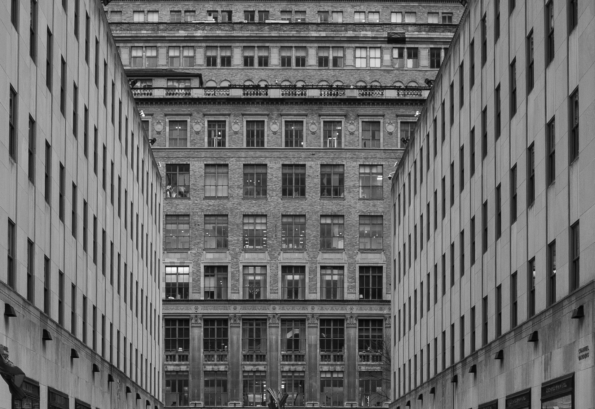 Black and white photograph of a narrow alleyway flanked by tall buildings with large windows.